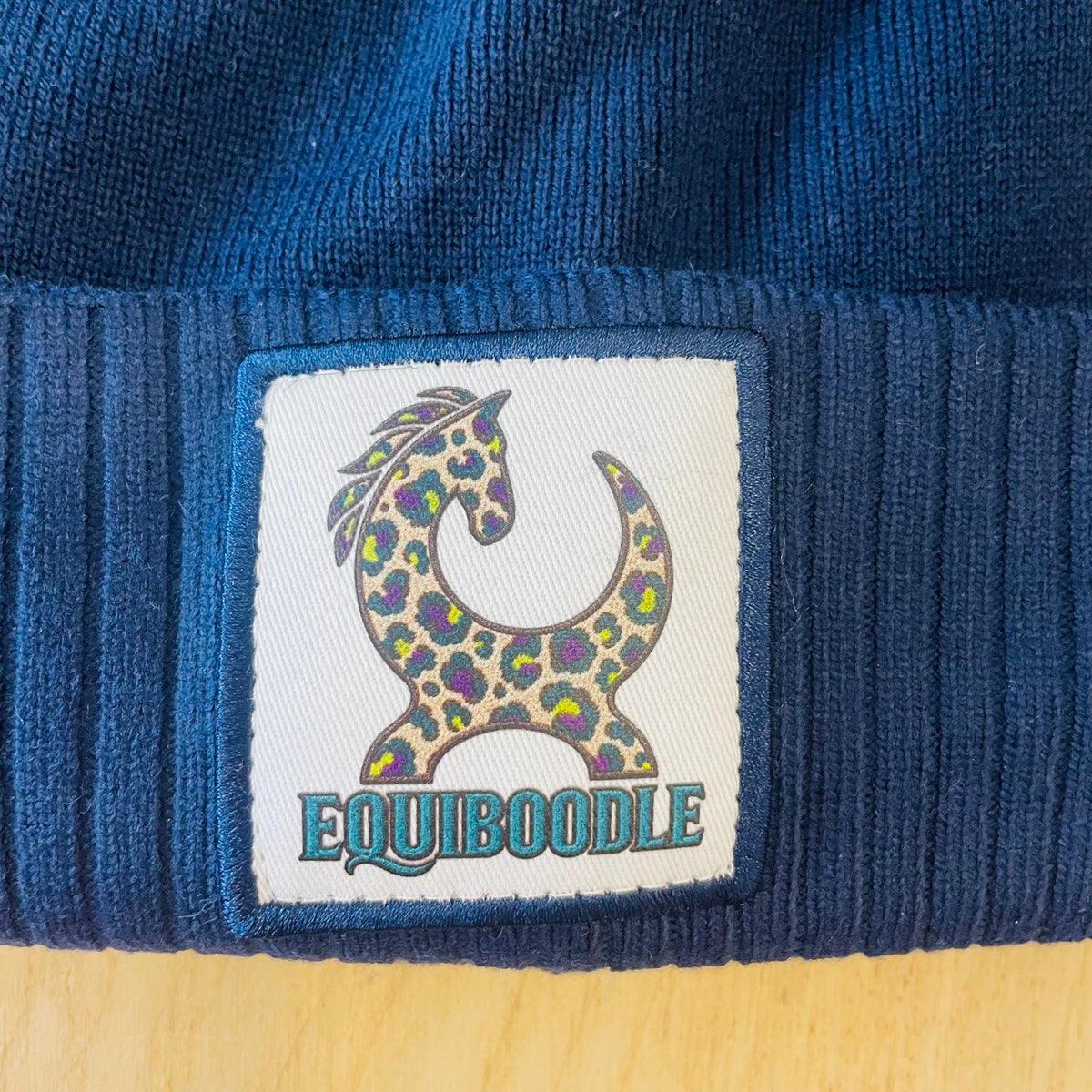 Close-up of Equiboodle colourful leopard horse patch on blue bobble hat