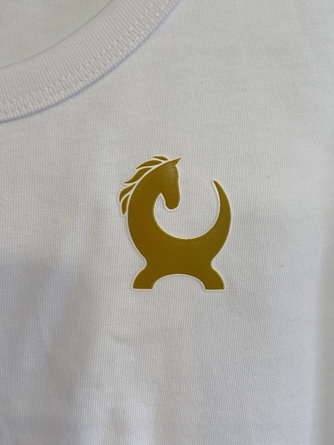 Close-up of gold Equiboodle horse emblem on white cotton vest
